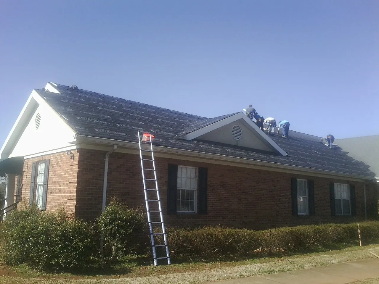 Crew tearing shingles off a brick ranch roof with a ladder set — Metal Roof Repair work by our crew in Greeleyville