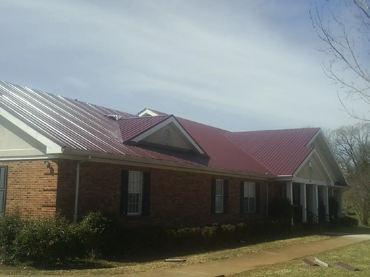 Red metal roof with gabled entries on a long brick building, from a Hail Damage Roof Repair job in Greeleyville