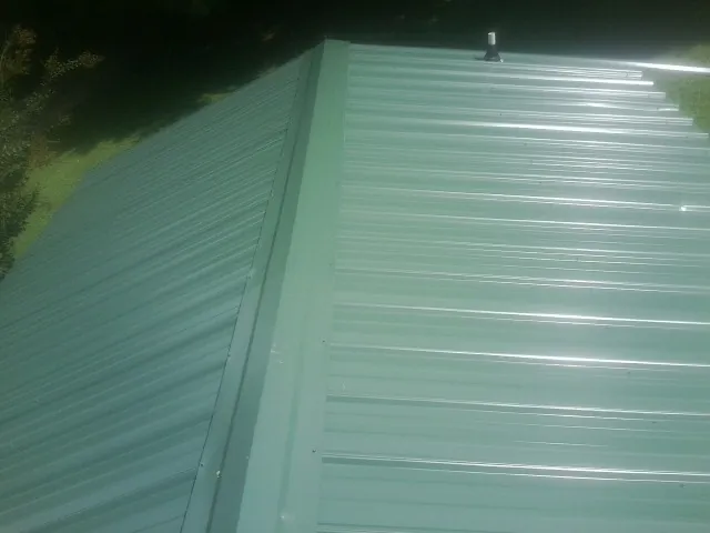 New green metal panels meeting at the ridge of a roof — Flat Roof Repair work by our crew in Greeleyville