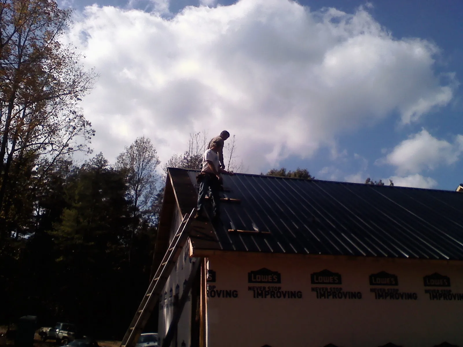 Roofer fastening dark metal panels high against a cloudy sky, from a Roof Inspection job in Greeleyville