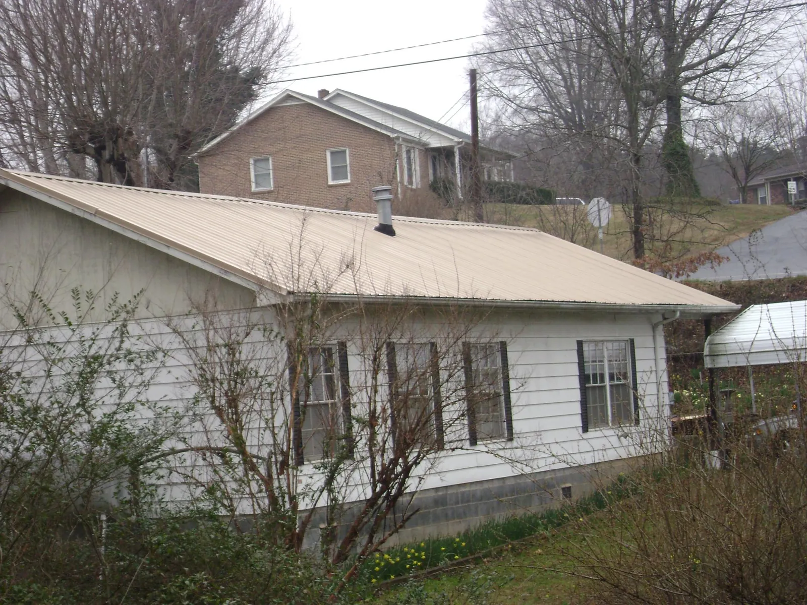 Tan metal roof on a white sided house set into a hillside — Commercial Roofing by Roofing Brothers in Greeleyville